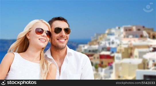 travel, tourism and summer holidays concept - happy couple hugging over santorini island background. happy couple in sunglasses over santorini island
