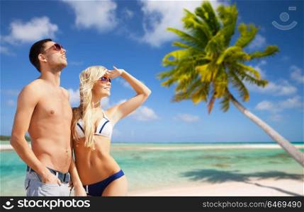 travel, tourism and summer holidays concept - happy couple in sunglasses at touristic resort over exotic tropical beach with palm tree background. happy couple on over exotic tropical beach
