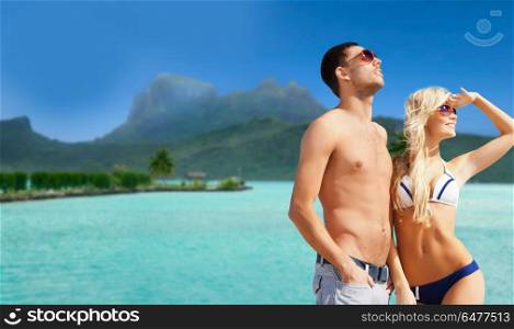 travel, tourism and summer holidays concept - happy couple in sunglasses at touristic resort over exotic bora bora island background. happy couple on over bora bora background. happy couple on over bora bora background