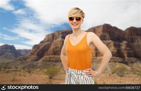 travel, tourism and summer holidays concept - happy smiling young woman in sunglasses over grand canyon national park background. happy smiling young woman