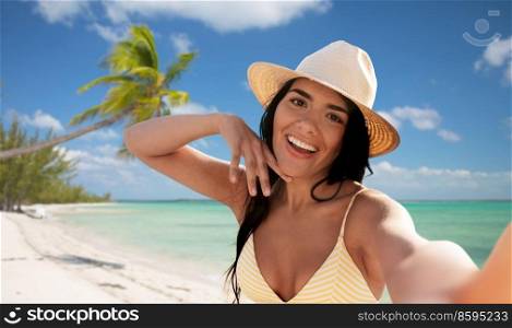 travel, tourism and summer holidays concept - happy smiling young woman in bikini swimsuit and straw hat taking selfie over tropical beach background in french polynesia. smiling woman in bikini taking selfie on beach