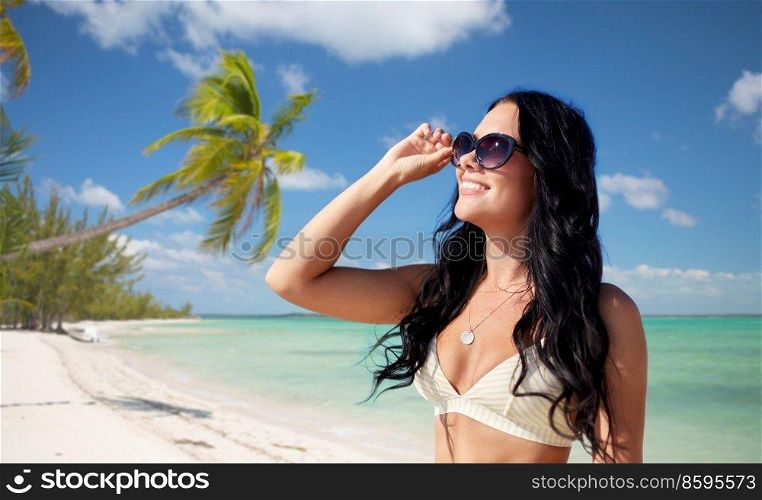 travel, tourism and summer holidays concept - happy smiling young woman in sunglasses and bikini swimsuit over tropical beach background in french polynesia. smiling young woman in sunglasses on exotic beach