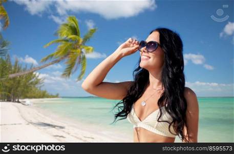 travel, tourism and summer holidays concept - happy smiling young woman in sunglasses and bikini swimsuit over tropical beach background in french polynesia. smiling young woman in sunglasses on exotic beach