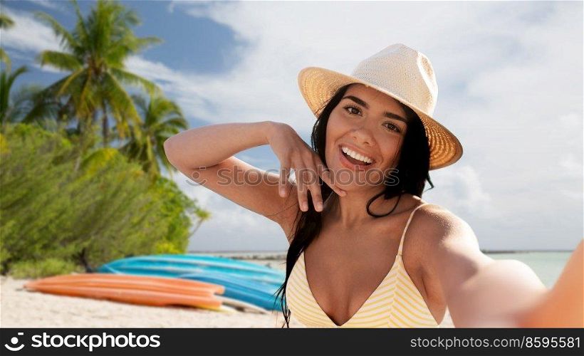 travel, tourism and summer holidays concept - happy smiling young woman in bikini swimsuit and straw hat taking selfie over tropical beach background in french polynesia. smiling woman in bikini taking selfie on beach