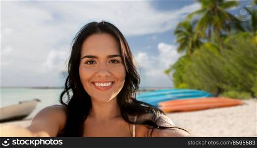 travel, tourism and summer holidays concept - happy smiling young woman in bikini swimsuit taking selfie over tropical beach background in french polynesia. smiling woman in bikini taking selfie on beach