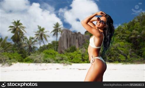 travel, tourism and summer holidays concept - happy smiling young woman in bikini swimsuit posing over seychelles island beach background. happy woman in bikini swimsuit on seychelles beach