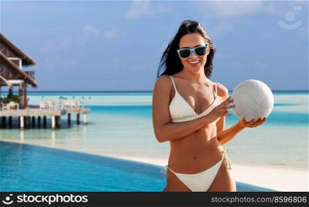 travel, tourism and summer holidays concept - happy smiling young woman in bikini swimsuit posing with volleyball over bungalow on tropical beach background in french polynesia. woman in bikini posing with volleyball on beach