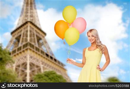 travel, tourism and summer holidays concept - happy young woman or teen girl in yellow dress with helium air balloons over paris eiffel tower background. happy woman in dress with helium air balloons