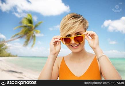 travel, tourism and summer holidays concept - portrait of happy smiling young woman in sunglasses over exotic tropical beach with palm trees background. portrait of smiling young woman in sunglasses
