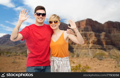 travel, tourism and summer holidays concept - smiling couple in sunglasses hugging and waving hands over grand canyon national park background. couple in sunglasses hugging and waving hands