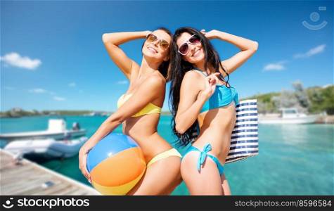 travel, tourism and summer vacation concept - beautiful happy women in bikinis with inflatable ball and bag posing over wooden pier and boat on tropical beach background in french polynesia. beautiful happy women with ball posing on beach