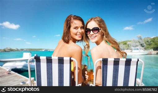 travel, tourism and summer vacation concept - beautiful happy women or female friends sunbathing on beach chairs over wooden pier and boat on tropical background in french polynesia. beautiful happy women sunbathing on beach chairs