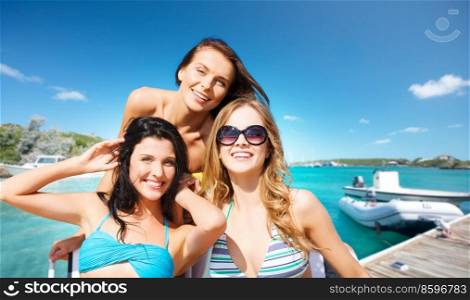 travel, tourism and summer vacation concept - beautiful happy women or female friends in bikinis and sunglasses over wooden pier and boat on tropical beach background in french polynesia. beautiful happy women in bikinis on beach