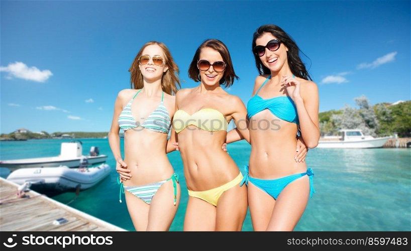 travel, tourism and summer vacation concept - beautiful happy women or female friends in bikinis and sunglasses posing over wooden pier and boat on tropical beach background in french polynesia. beautiful happy women in bikinis posing on beach