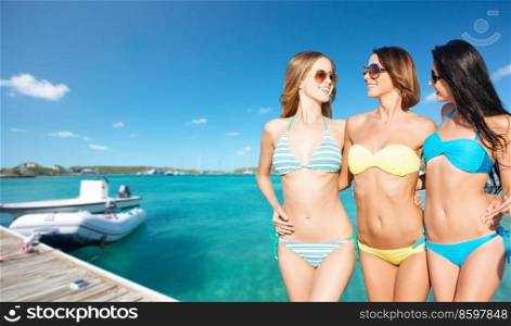 travel, tourism and summer vacation concept - beautiful happy women or female friends in bikinis and sunglasses posing over wooden pier and boat on tropical beach background in french polynesia. beautiful happy women in bikinis posing on beach