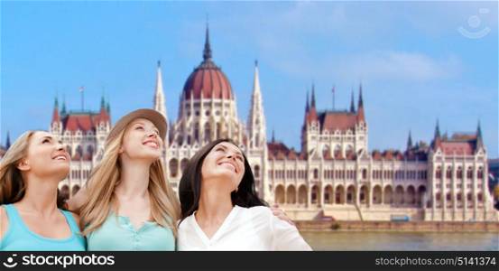 travel, tourism and summer vacation concept - group of happy smiling women or friends over house of parliament in budapest. happy women over house of parliament in budapest