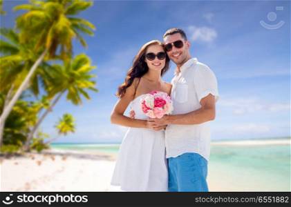 travel, tourism and summer vacation concept - happy smiling couple with bunch of flowers hugging over tropical beach background in french polynesia. happy couple with flowers over tropical beach. happy couple with flowers over tropical beach