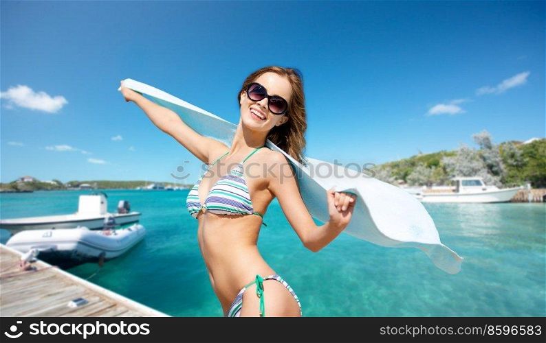 travel, tourism and summer vacation concept - happy smiling woman in bikini with towel posing over wooden pier and boat on tropical beach background in french polynesia. happy smiling woman in bikini posing on beach