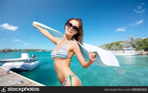 travel, tourism and summer vacation concept - happy smiling woman in bikini with towel posing over wooden pier and boat on tropical beach background in french polynesia. happy smiling woman in bikini posing on beach