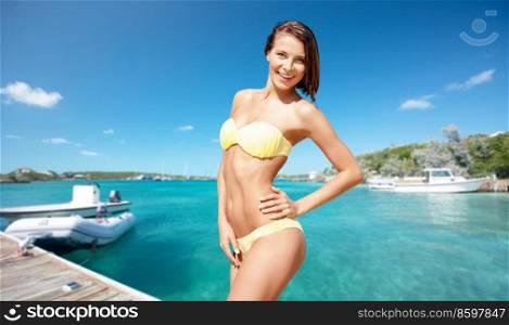 travel, tourism and summer vacation concept - happy smiling woman in bikini posing over wooden pier and boat on tropical beach background in french polynesia. happy smiling woman in bikini posing on beach