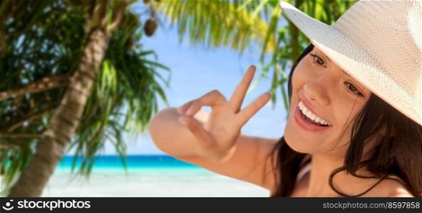 travel, tourism and summer vacation concept - happy smiling woman in straw hat showing peace gesture over tropical beach and palm trees background in french polynesia. smiling woman in straw hat showing peace on beach