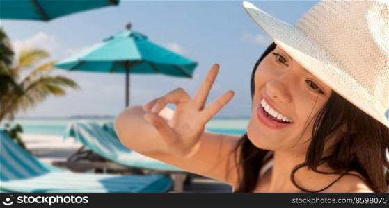 travel, tourism and summer vacation concept - happy smiling woman in straw hat showing peace gesture over tropical beach background in french polynesia. smiling woman in straw hat showing peace on beach