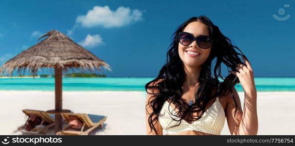 travel, tourism and summer vacation concept - happy smiling young woman in sunglasses and bikini swimsuit over tropical beach background in french polynesia. smiling young woman in sunglasses on summer beach