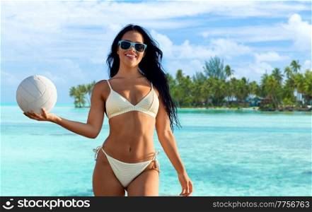 travel, tourism and summer vacation concept - happy smiling young woman in bikini swimsuit posing with volleyball over tropical beach background in french polynesia. woman in bikini posing with volleyball on beach