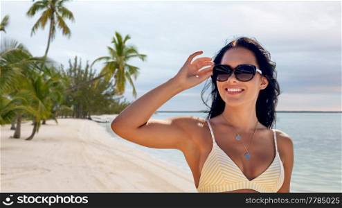 travel, tourism and summer vacation concept - happy smiling young woman in sunglasses and bikini swimsuit over tropical beach background in french polynesia. smiling young woman in sunglasses on summer beach