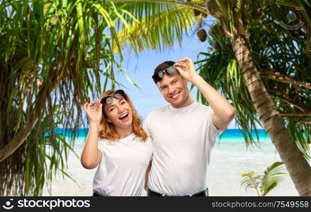 travel, tourism and summer vacation concept - portrait of happy couple in white t-shirts and sunglasses over tropical beach background in french polynesia. happy couple in sunglasses on tropical beach