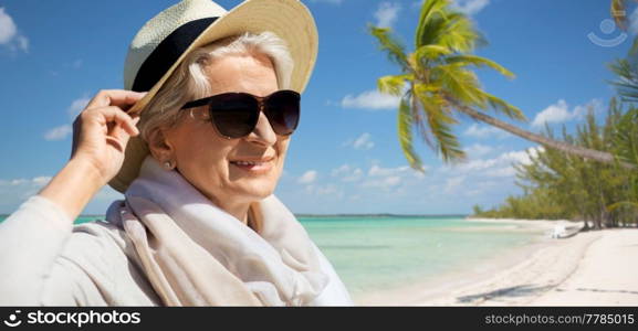 travel, tourism and summer vacation concept - portrait of happy senior woman in sunglasses and straw hat over tropical beach background in french polynesia. happy senior woman in sunglasses and hat on beach