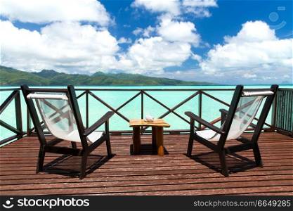 travel, tourism and summer vacation concept - two chaise longues and table on wooden terrace in french polynesia. two chaise longues on terrace in french polynesia