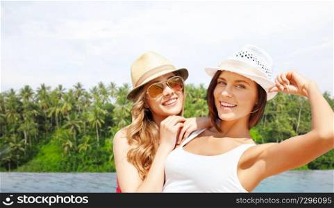 travel, tourism and summer vacation concept - young women or teenage girls in hats over infinity edge pool and palms in sri lanka background. teenage girls over infinity edge pool in sri lanka