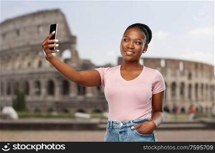 travel, tourism and technology c concept - happy african american woman taking selfie by smartphone over coliseum background. african american woman taking selfie over coliseum