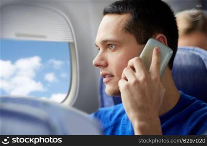travel, tourism and technology concept - close up of young man calling on smartphone in plane and looking into porthole. young man calling on smartphone in plane. young man calling on smartphone in plane