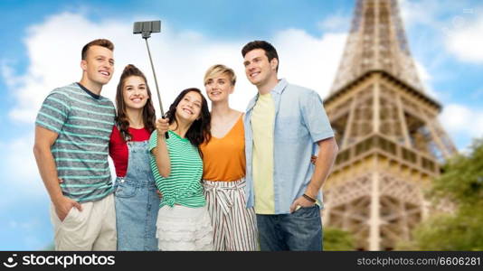 travel, tourism and technology concept - group of happy smiling friends taking selfie by smartphone over eiffel tower background. friends taking selfie by monopod over eiffel tower