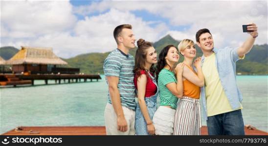 travel, tourism and technology concept - group of happy smiling friends taking selfie by smartphone over bora bora background. friends taking selfie by smartphone over bora bora