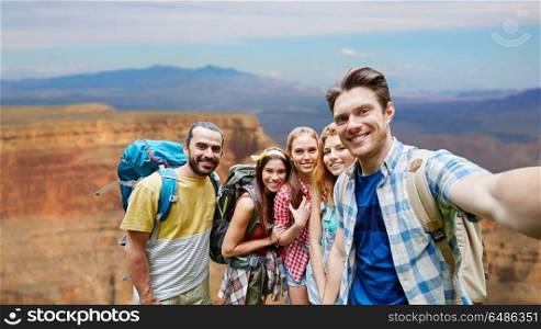 travel, tourism and technology concept - group of smiling friends or travelers with backpacks taking selfie over rocks of grand canyon national park background. happy travelers taking selfie at grand canyon. happy travelers taking selfie at grand canyon