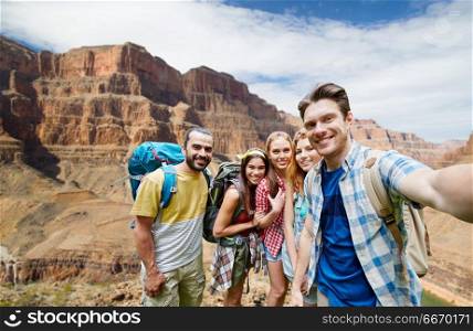 travel, tourism and technology concept - group of smiling friends or travelers with backpacks taking selfie over rocks of grand canyon national park background. happy travelers taking selfie at grand canyon. happy travelers taking selfie at grand canyon