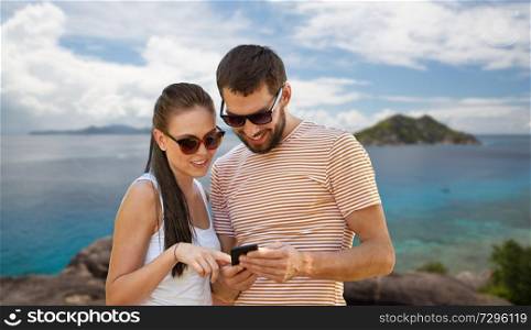 travel, tourism and technology concept - happy couple with smartphone over tropical beach on seychelles island background. happy couple with smartphone on seychelles island