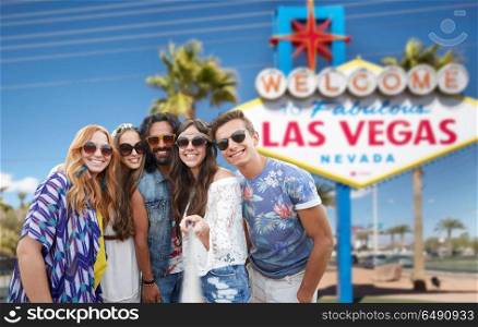 travel, tourism and technology concept - smiling young hippie friends taking picture by smartphone on selfie stick over welcome to fabulous las vegas sign background. friends taking selfie by monopod at las vegas sign. friends taking selfie by monopod at las vegas sign