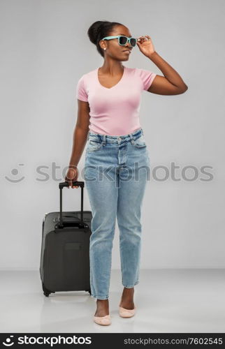 travel, tourism and vacation concept - happy african american young woman in sunglasses with carry-on bag over grey background. happy african woman in sunglasses with travel bag