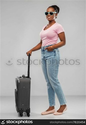 travel, tourism and vacation concept - happy african american young woman in sunglasses with carry-on bag over grey background. happy african woman in sunglasses with travel bag