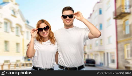 travel, tourism and vacation concept - happy couple in white t-shirts and sunglasses over city street background. happy couple in t-shirts and sunglasses in city