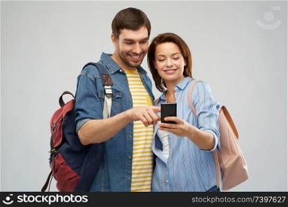 travel, tourism and vacation concept - happy couple of tourists with smartphone and backpacks over grey background. happy couple of tourists with smartphone