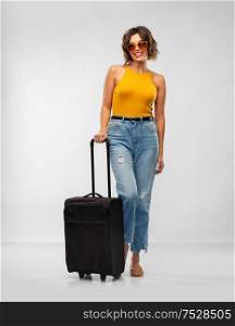 travel, tourism and vacation concept - happy laughing young woman in mustard yellow top with carry-on bag over grey background. happy young woman in sunglasses with travel bag