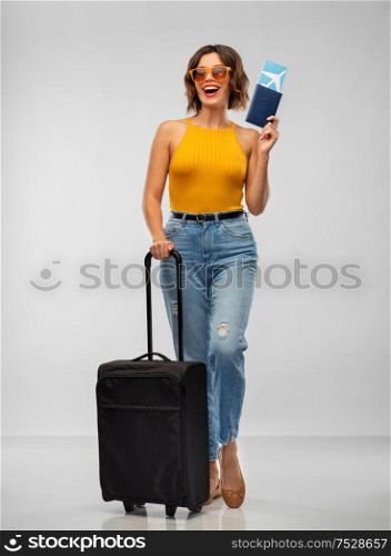 travel, tourism and vacation concept - happy laughing young woman in mustard yellow top with air ticket, passport and carry-on bag over grey background. happy young woman with air ticket and travel bag