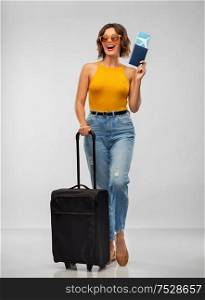 travel, tourism and vacation concept - happy laughing young woman in mustard yellow top with air ticket, passport and carry-on bag over grey background. happy young woman with air ticket and travel bag