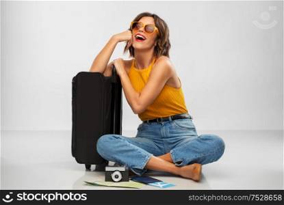 travel, tourism and vacation concept - happy laughing young woman in mustard yellow top with air ticket, camera, map and carry-on bag over grey background. woman with travel bag, air ticket, map and camera