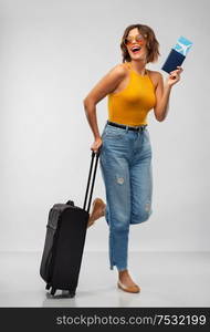 travel, tourism and vacation concept - happy laughing young woman in mustard yellow top with air ticket, passport and carry-on bag over grey background. happy young woman with air ticket and travel bag